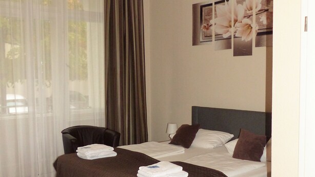 Een hotelkamer met een groot bed, een stoel, een nachtkastje en een raam met gordijnen.