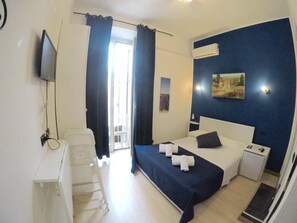A hotel room with a bed, bedside table, a desk with a chair, a television, and a window with curtains. - Julius Caesar 183 (Rome)