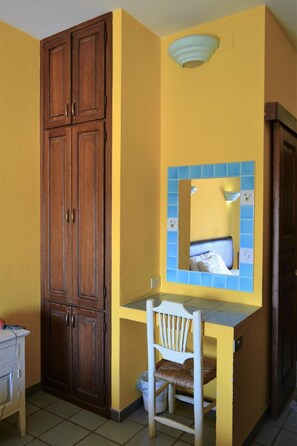 Una habitación con un armario de madera, un escritorio pequeño con silla, y un espejo con marco azul.