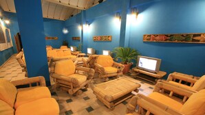 A room with several wicker chairs and sofas, a television, and wall-mounted lights. - Hotel Dell'Ancora (Villasimius)
