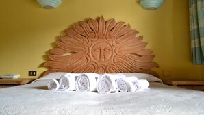 A bed with a sun-shaped headboard, rolled towels, and two wall-mounted light fixtures. - Hotel Dell'Ancora (Villasimius)