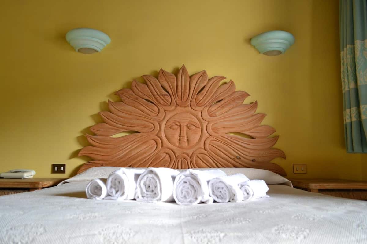 Un letto con testiera a forma di sole, asciugamani arrotolati e due lampade fissate alla parete.