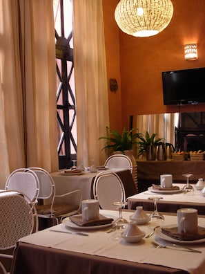 Un espace repas avec des tables préparées pour deux personnes, des chaises blanches et un lustre.
