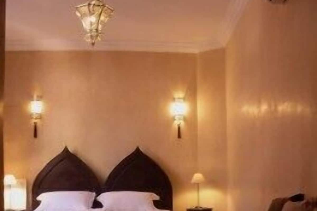 A hotel room with a large bed, two bedside tables, a chandelier, and a small table with a lamp.