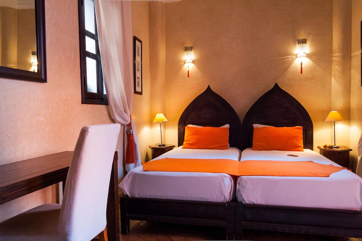 A double bed with two pillows, a nightstand with a lamp, a chair, and a mirror on the wall.