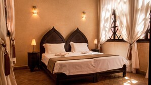 A neatly made bed with a dark wooden headboard, two bedside lamps, and a window with curtains. - Riad Aderbaz (Marrakech)
