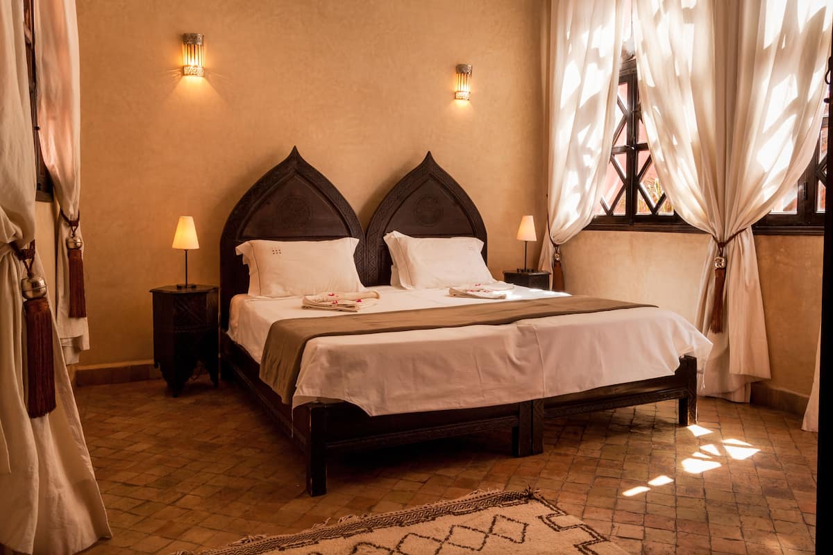 A neatly made bed with a dark wooden headboard, two bedside lamps, and a window with curtains.