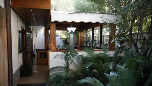 A covered outdoor area with wooden beams, a black mat at the entrance, and various plants including palm trees. - Villa Alba Boutique Hotel (Pescara)