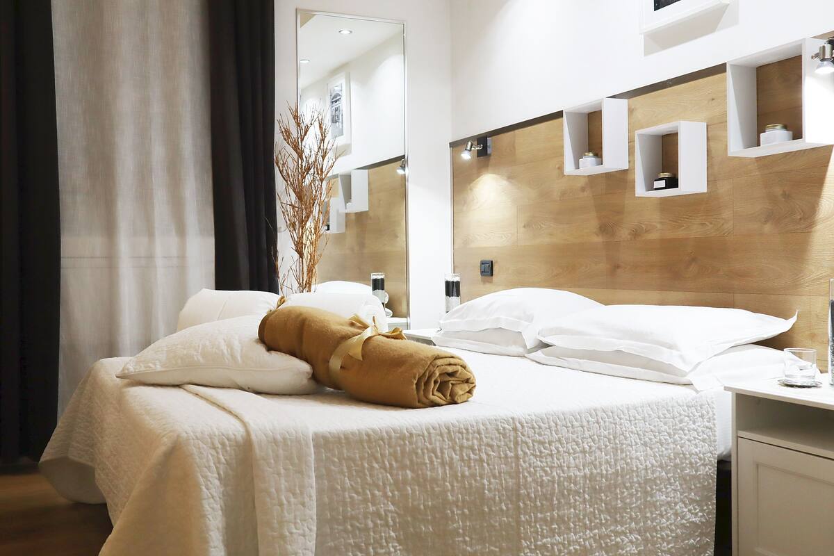 A hotel room with a bed, a mirror, a wooden headboard, and a small table with a glass.