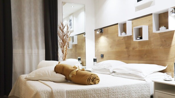 A hotel room with a bed, a mirror, a wooden headboard, and a small table with a glass. - Villa Alba Boutique Hotel (Pescara)