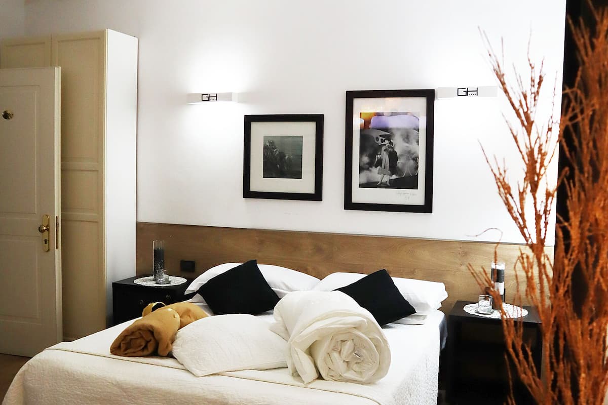 A neatly made bed with white linens and black pillows, a bedside table with a lamp, and framed pictures on the wall.