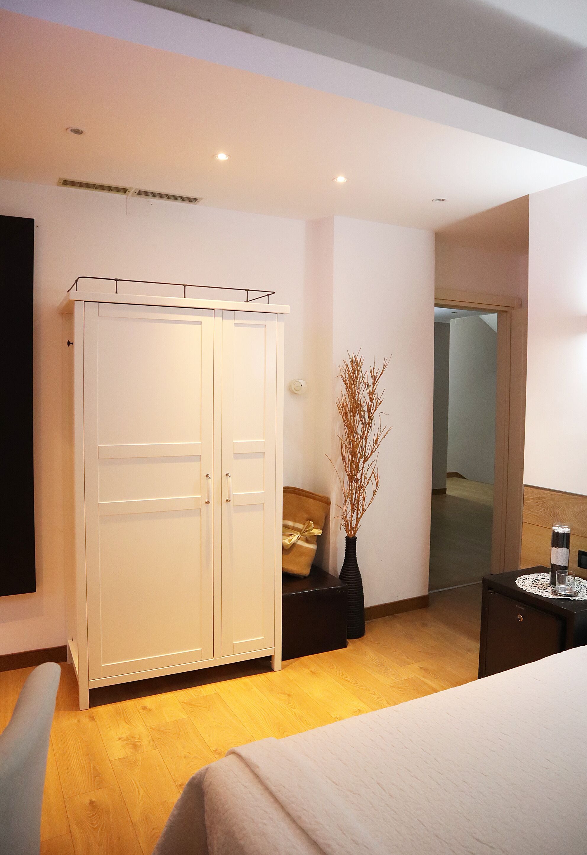 Una habitación de hotel moderna con un armario grande, una mesita de noche con un jarrón y suelo de madera.