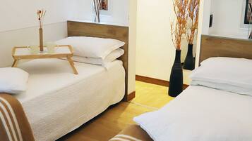 A hotel room with two beds, a wooden floor, white bedding, and two black vases with branches.