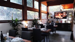 A dining area with tables set for a meal, large windows, and a kitchen area visible in the background. - Villa Alba Boutique Hotel (Pescara)