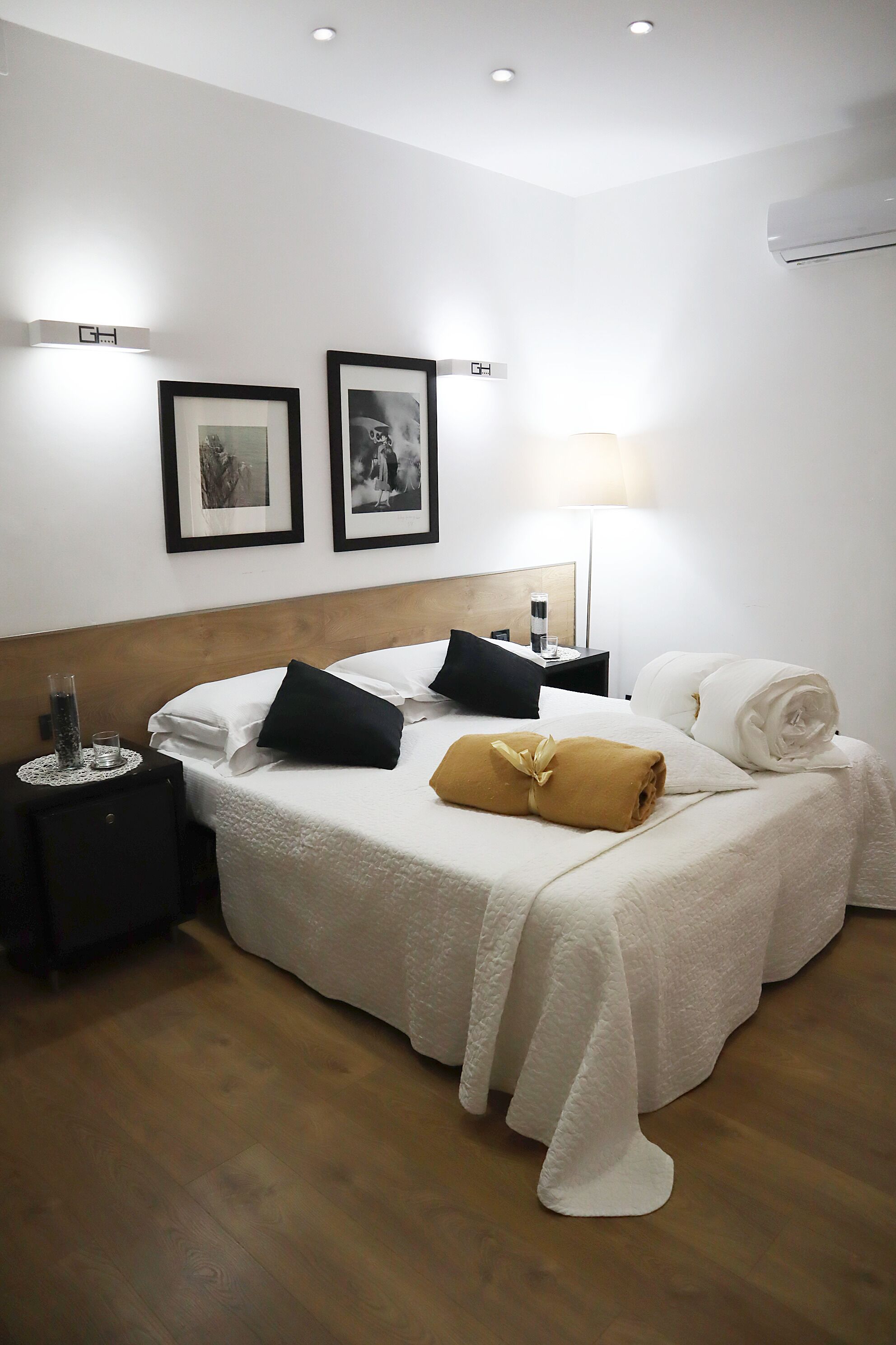 Ein ordentlich eingerichtetes Hotelzimmer mit einem Bett, Nachttischen, gerahmten Bildern an der Wand und einer Lampe.