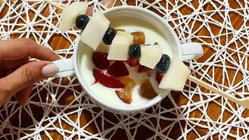 Una taza blanca con asa, llena de un líquido blanco, posiblemente leche o yogur, y adornada con diversas frutas y una cuchara.