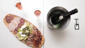Une planche de charcuterie avec divers types de viandes et de fromages, deux verres de vin rosé et une bouteille de champagne Ferrari dans une carafe.