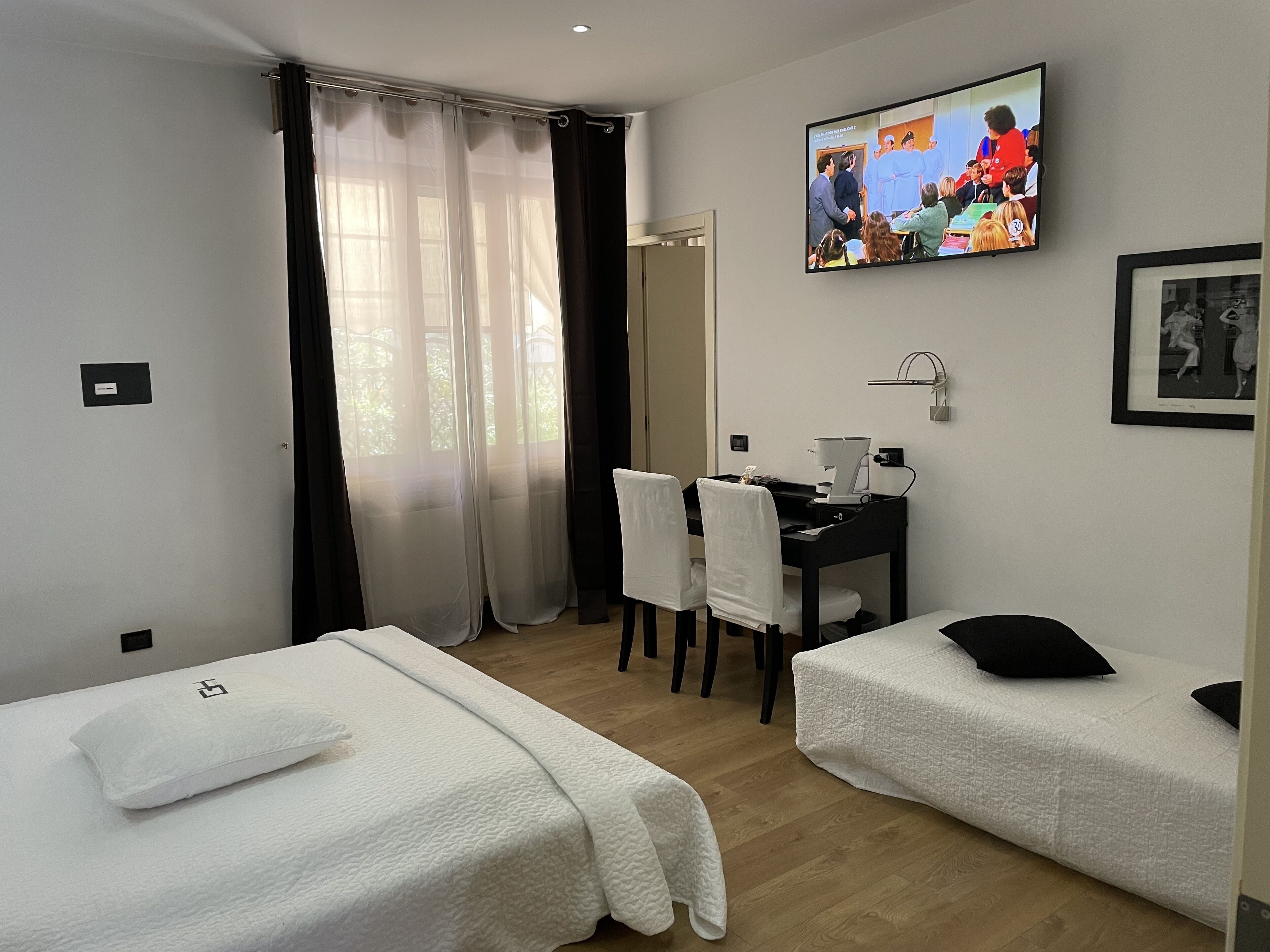 Ein Hotelzimmer mit zwei Einzelbetten, einem Schreibtisch mit Stuhl, einem Fernseher und einem Fenster mit Vorhängen.