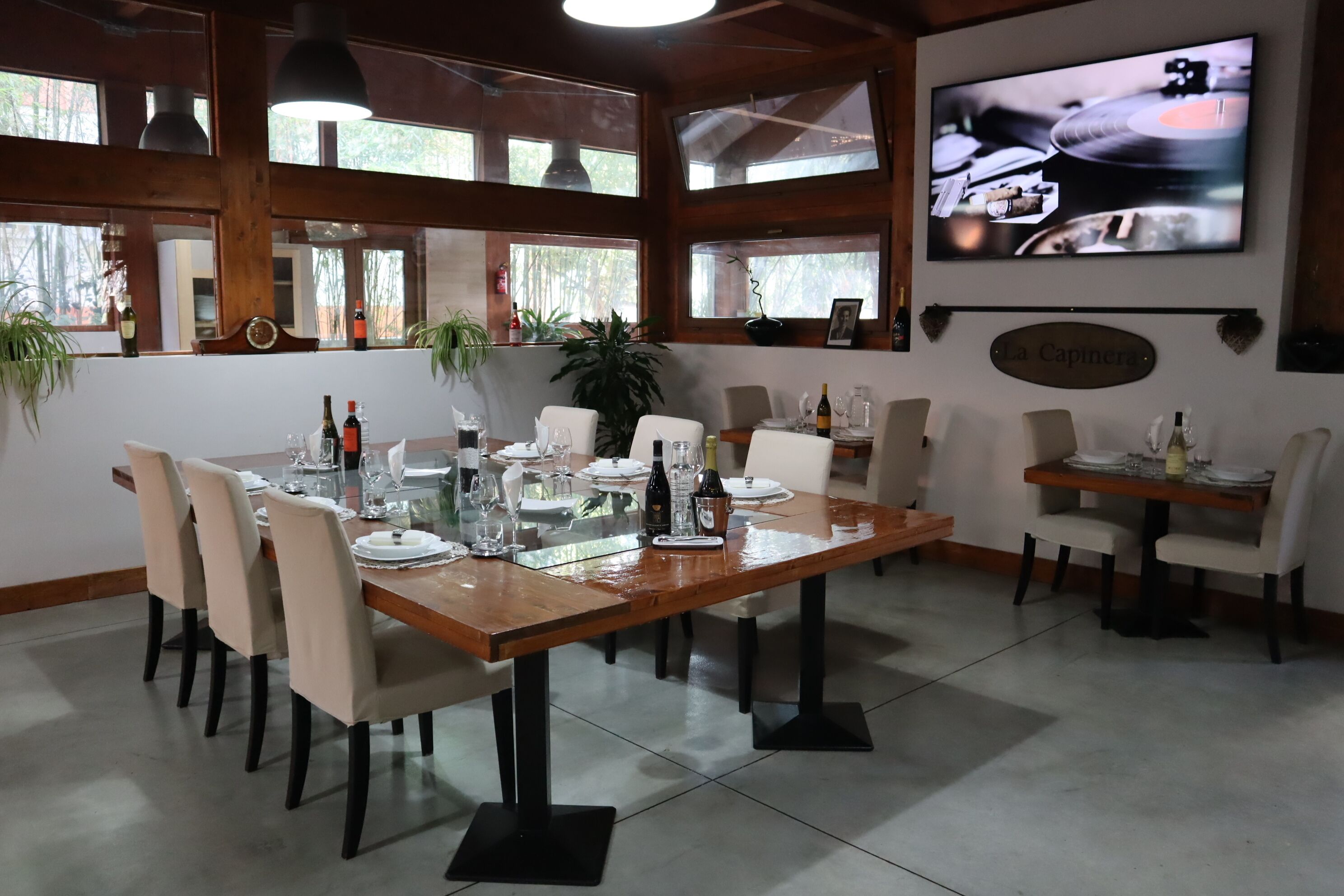 Un coin repas avec une table en bois dressée pour six personnes, entourée de chaises. On peut voir des bouteilles et des verres sur la table, et un téléviseur fixé au mur qui diffuse un clip vidéo.