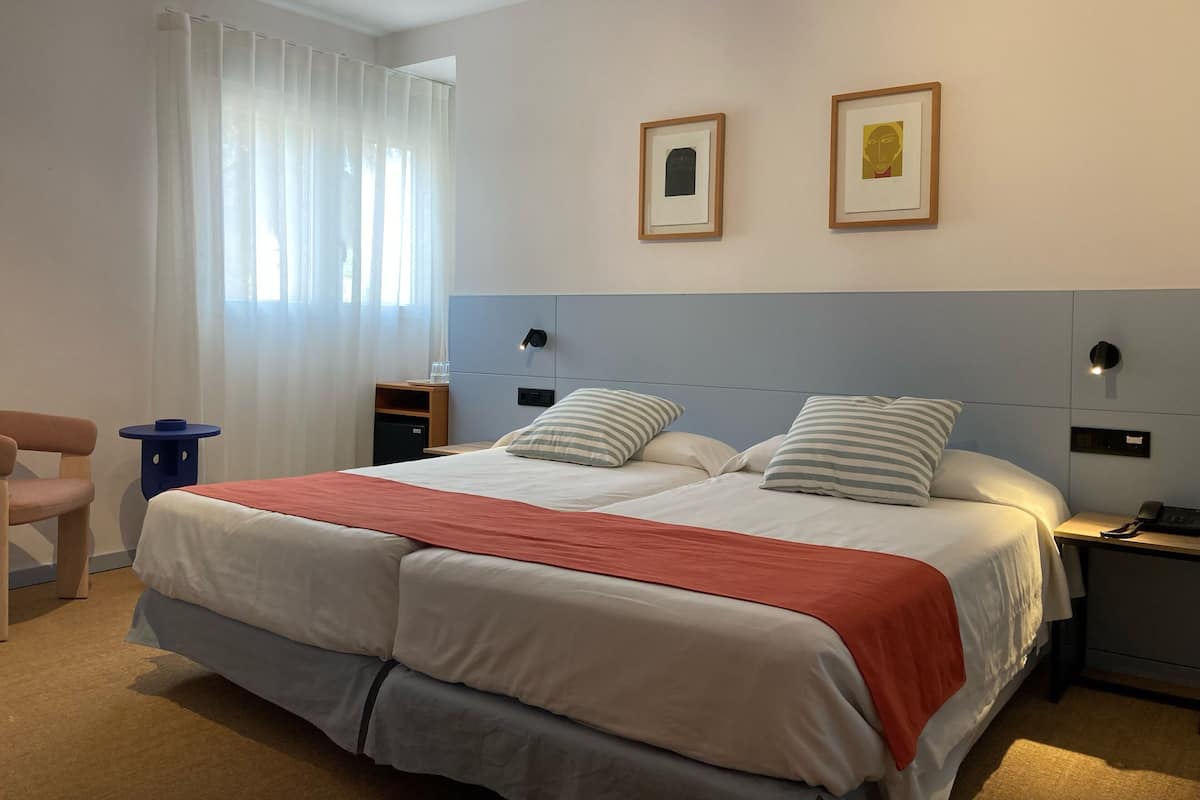 Een hotelkamer met een groot bed, een bureau, een stoel en twee ingelijste foto's aan de muur.