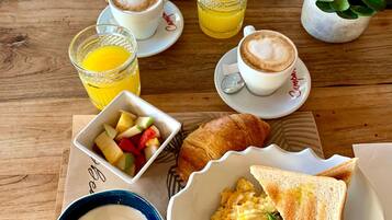 Una mesa de desayuno con cruasanes, huevos revueltos, tostadas, fruta, café y jugo.