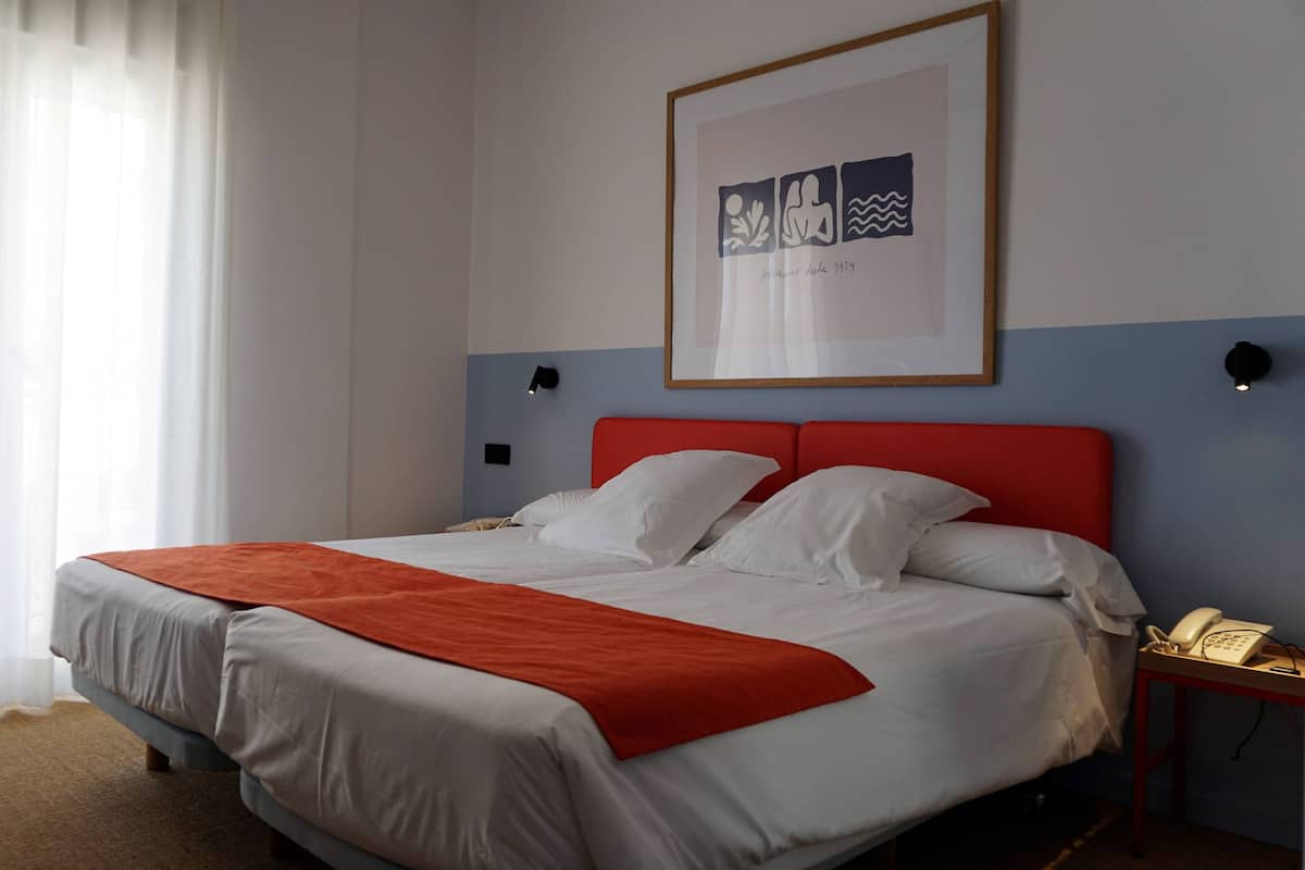 Een hotelkamer met een bed, een rode hoofdbord, een ingelijst schilderij aan de muur en een telefoon op een nachtkastje.