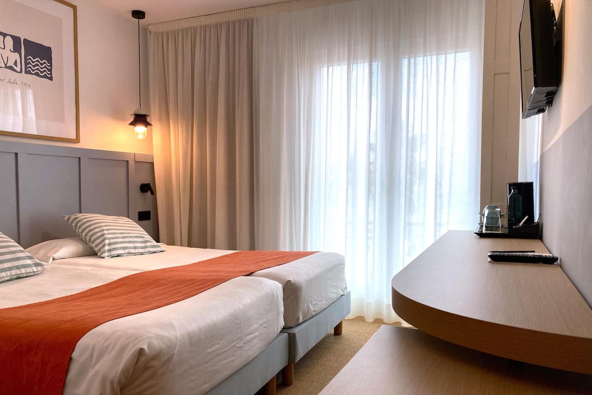 Een hotelkamer met twee bedden, een bureau, een televisie en een raam met gordijnen.