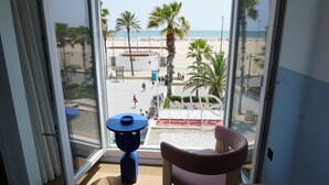 A room with a large window overlooking a beach, a small table, and a chair. - Hotel Miramar Valencia (Valencia)
