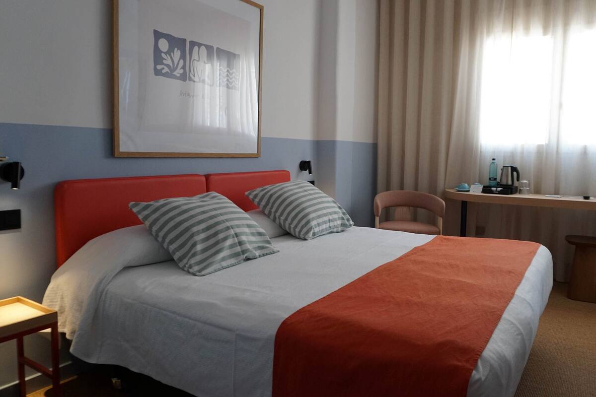 Een hotelkamer met een bed, een bureau, een stoel en een ingelijste foto aan de muur.