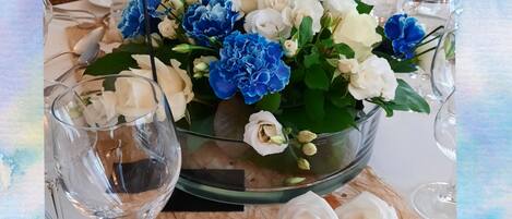 Une table dressée avec un vase en verre rempli de fleurs, des verres à vin et des couverts.