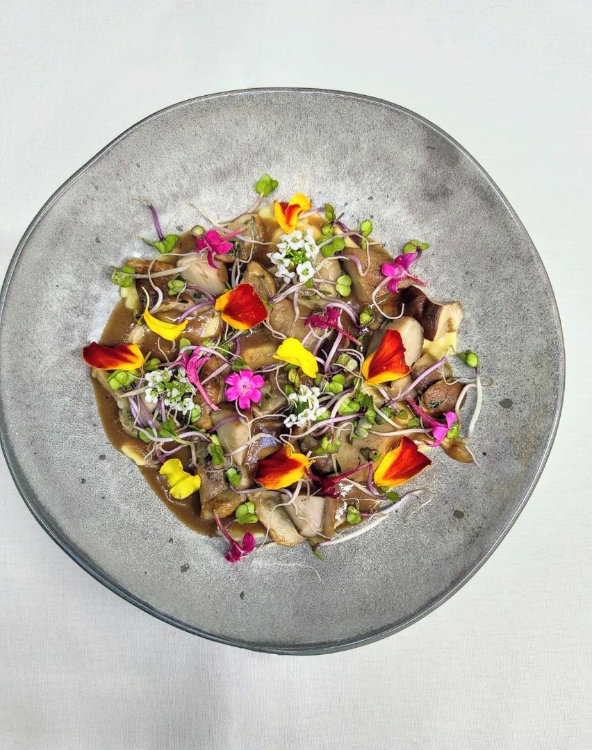 Un plato redondo y texturizado con una ensalada colorida de diversas verduras y flores.