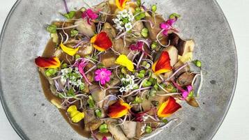 Un plato redondo y texturizado con una ensalada colorida de diversas verduras y flores.