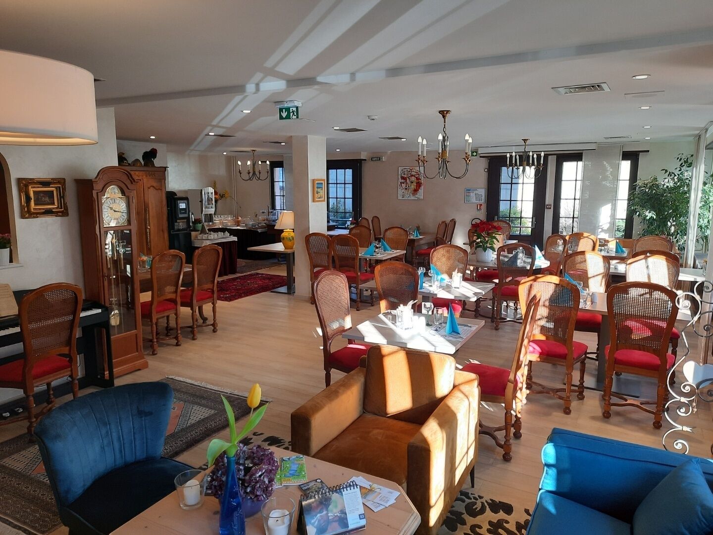 A spacious hotel lobby with multiple dining areas, wooden furniture, and large windows allowing natural light.