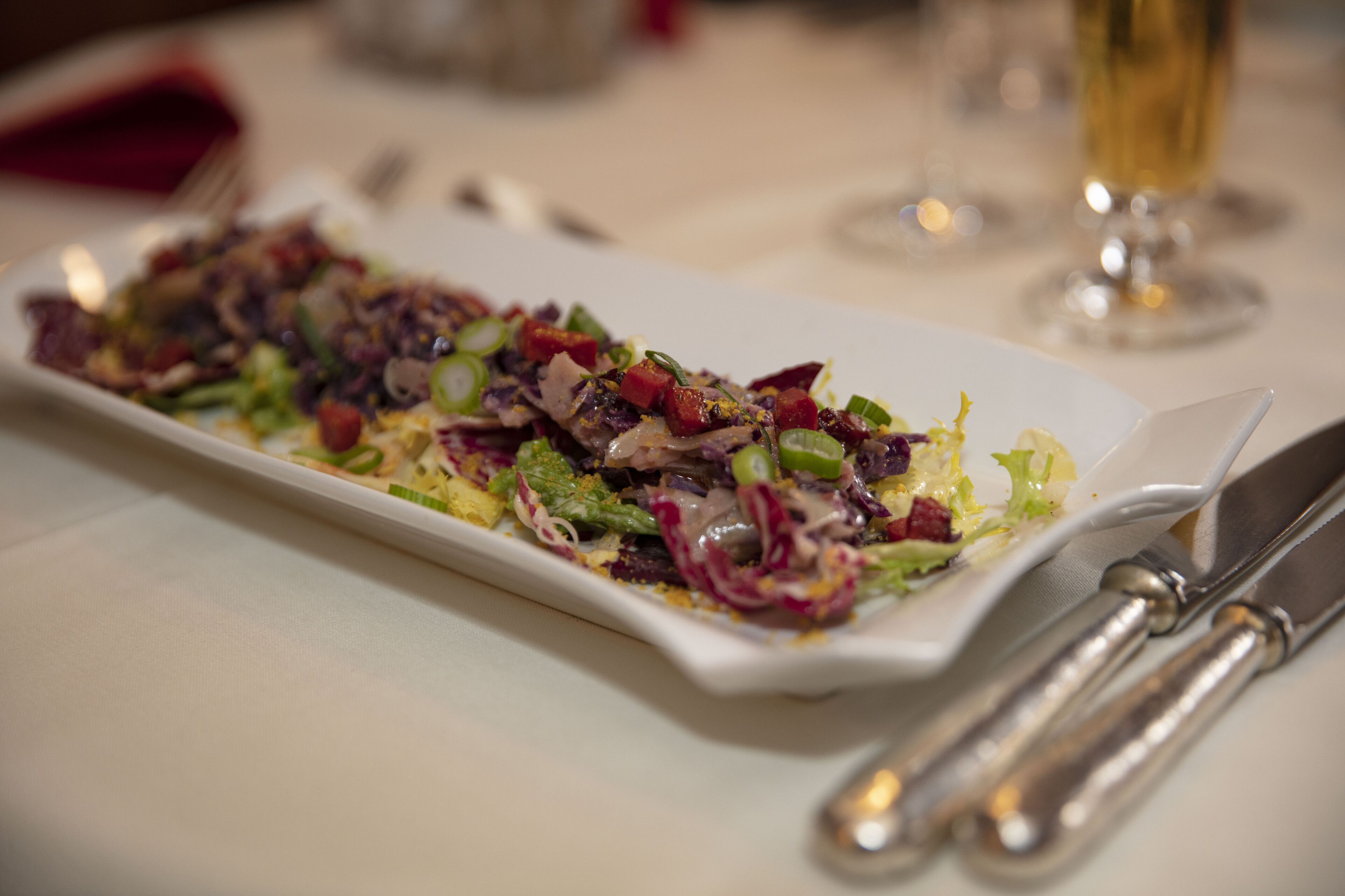 A rectangular white plate with a colorful salad, a fork, and a knife on a table.