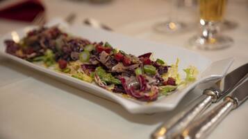 A rectangular white plate with a colorful salad, a fork, and a knife on a table.
