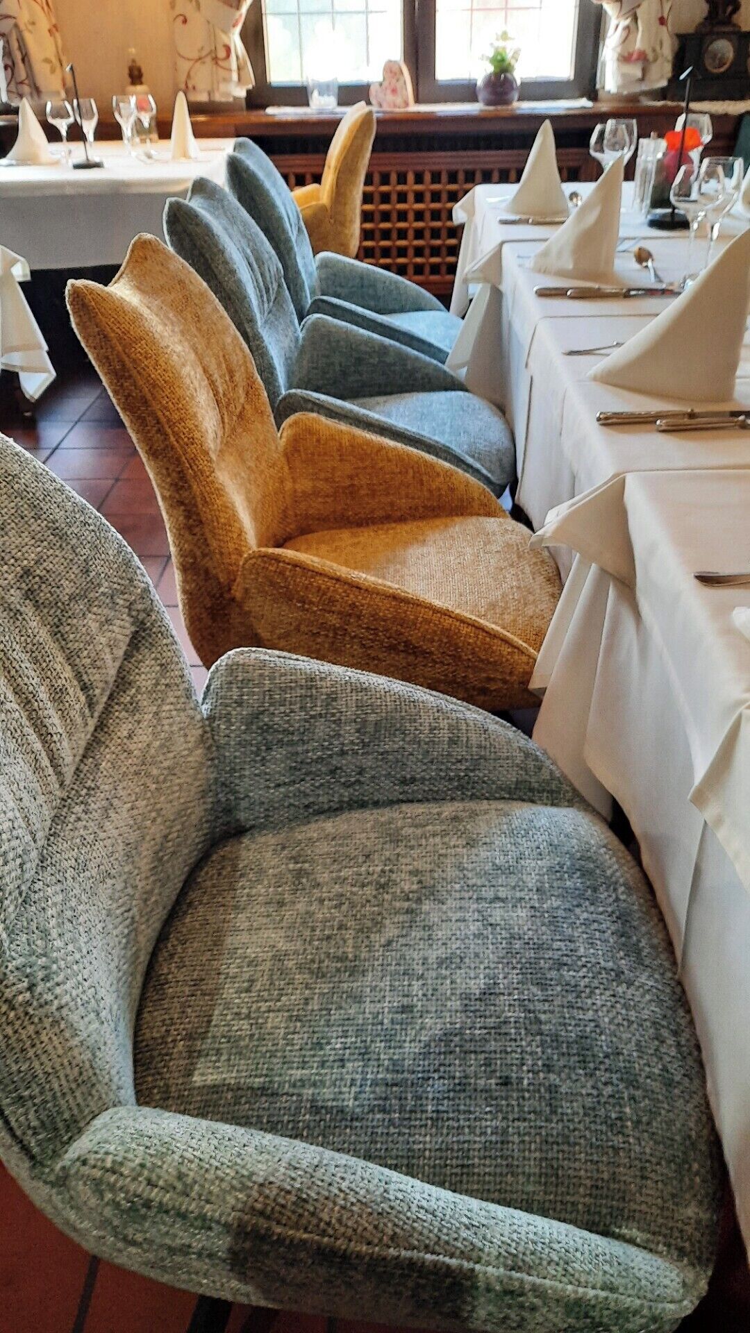 Una hilera de sillas tapizadas con tela texturizada, dispuestas en un comedor con mesas preparadas para una comida.