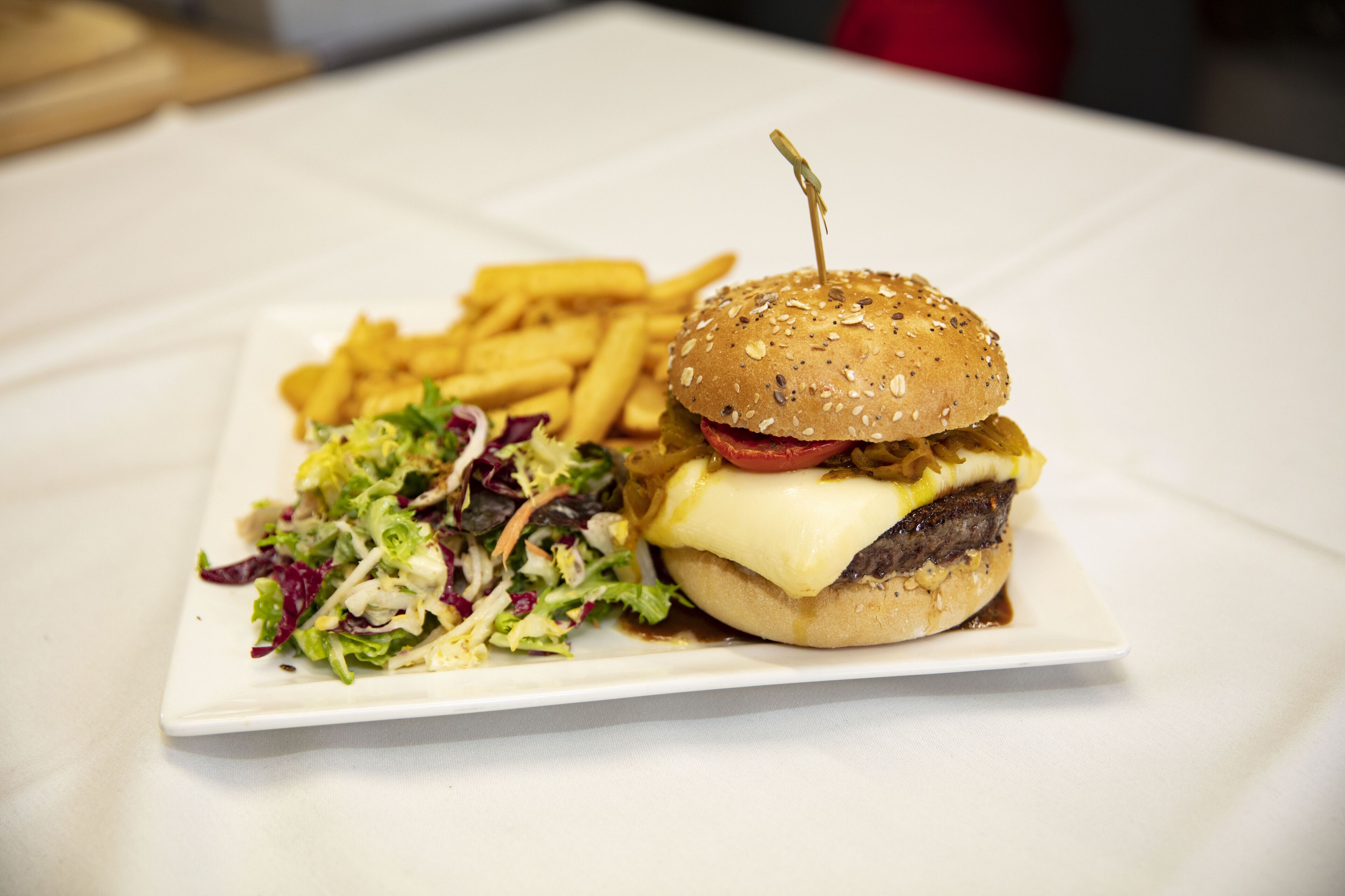 Un repas composé d’un hamburger, de frites et d’une salade, le tout servi dans une assiette blanche.