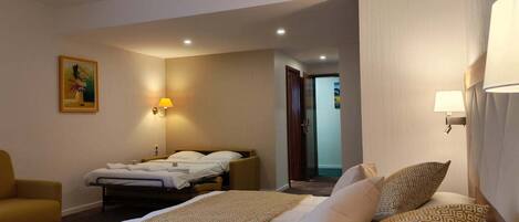 A hotel room with a large bed, a smaller bed, a chair, and a painting on the wall.