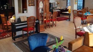 A spacious hotel lobby with a piano, multiple seating areas, a large wooden cabinet, and a modern chandelier. - Hostellerie Saint Florent (Oberhaslach)