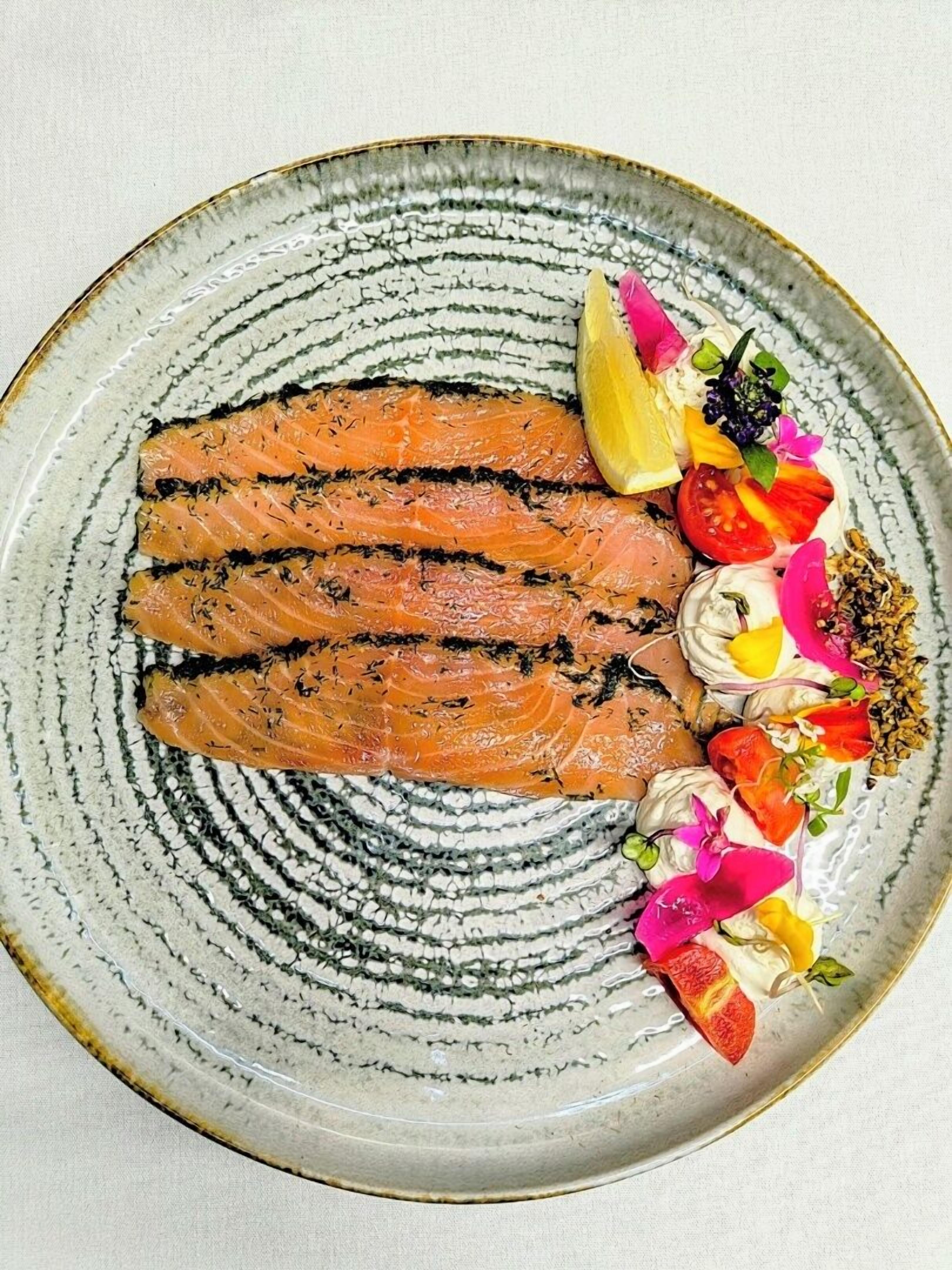 Une assiette contenant du saumon grillé, un quartier de citron et une garniture colorée.