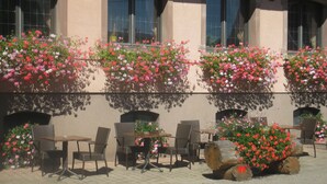 An outdoor seating area with tables and chairs, surrounded by flower boxes with pink and red flowers. - Hostellerie Saint Florent (Oberhaslach)