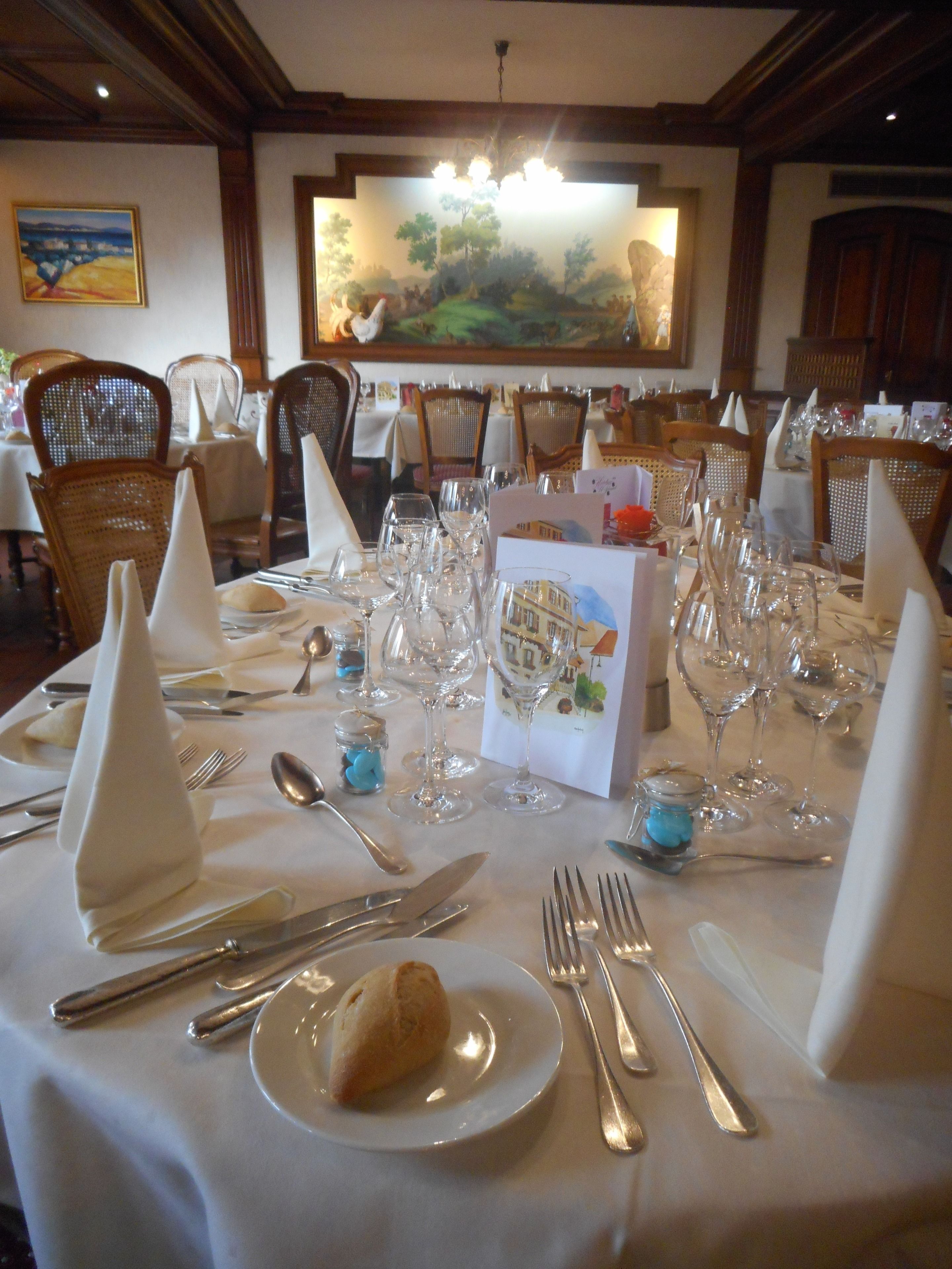 Une table à manger dressée pour un repas, avec plusieurs verres à vin, des fourchettes, des couteaux et une assiette contenant une pâtisserie.