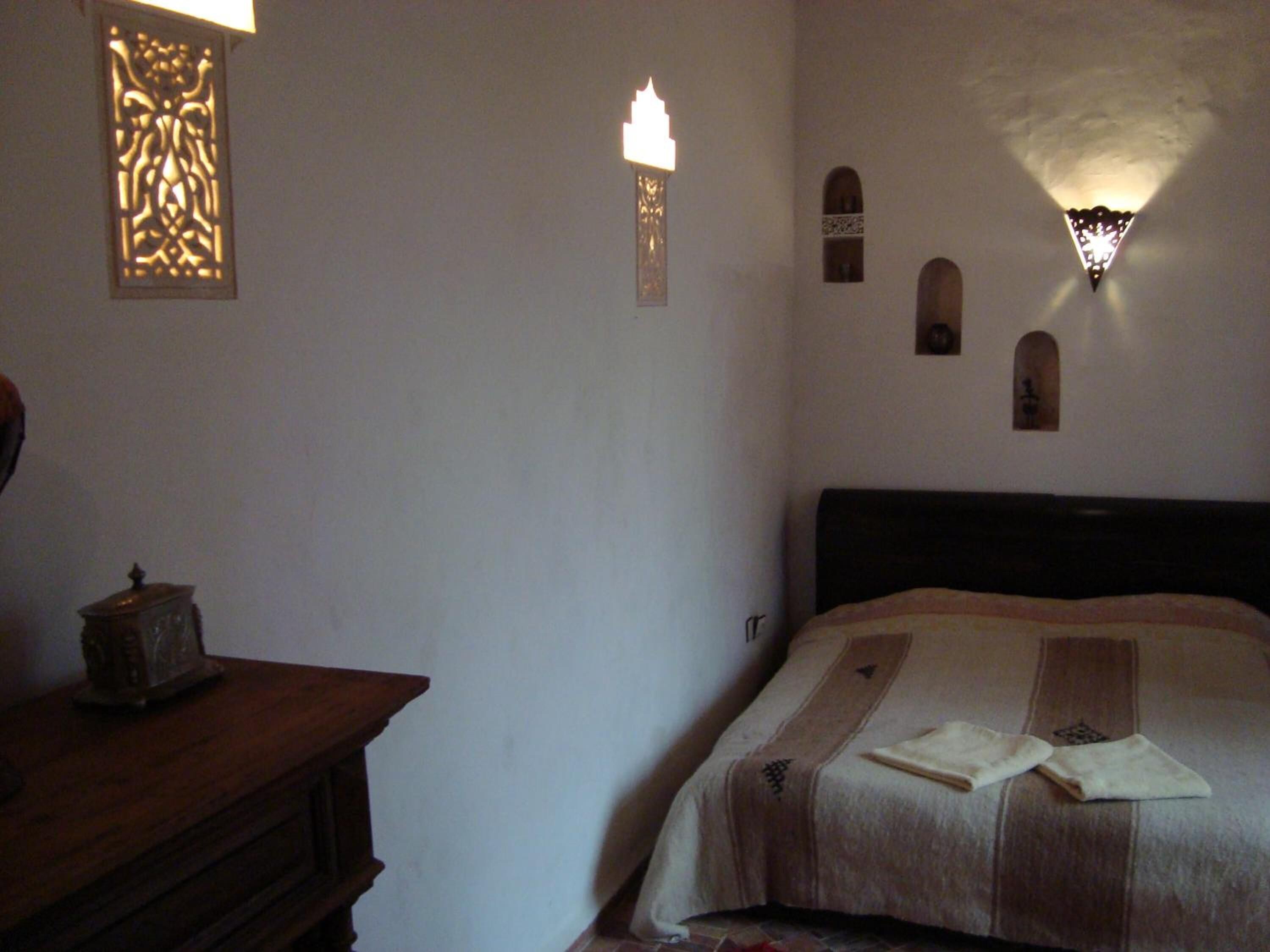 A bedroom with a bed, a wooden dresser, and decorative wall sconces.