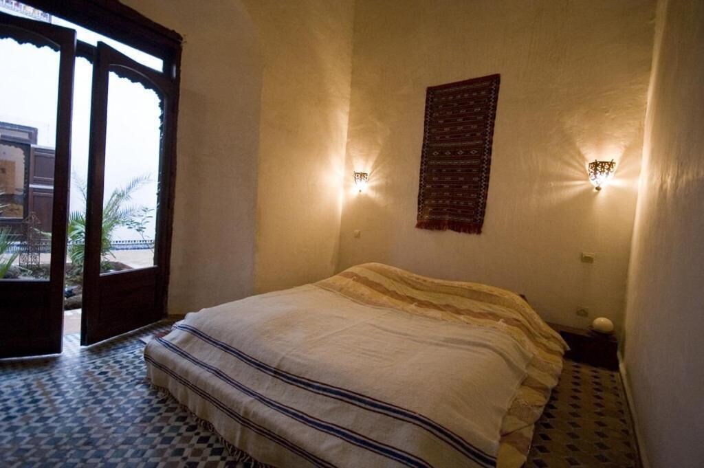 A bedroom with a bed, a patterned wall hanging, and two wall-mounted lights.