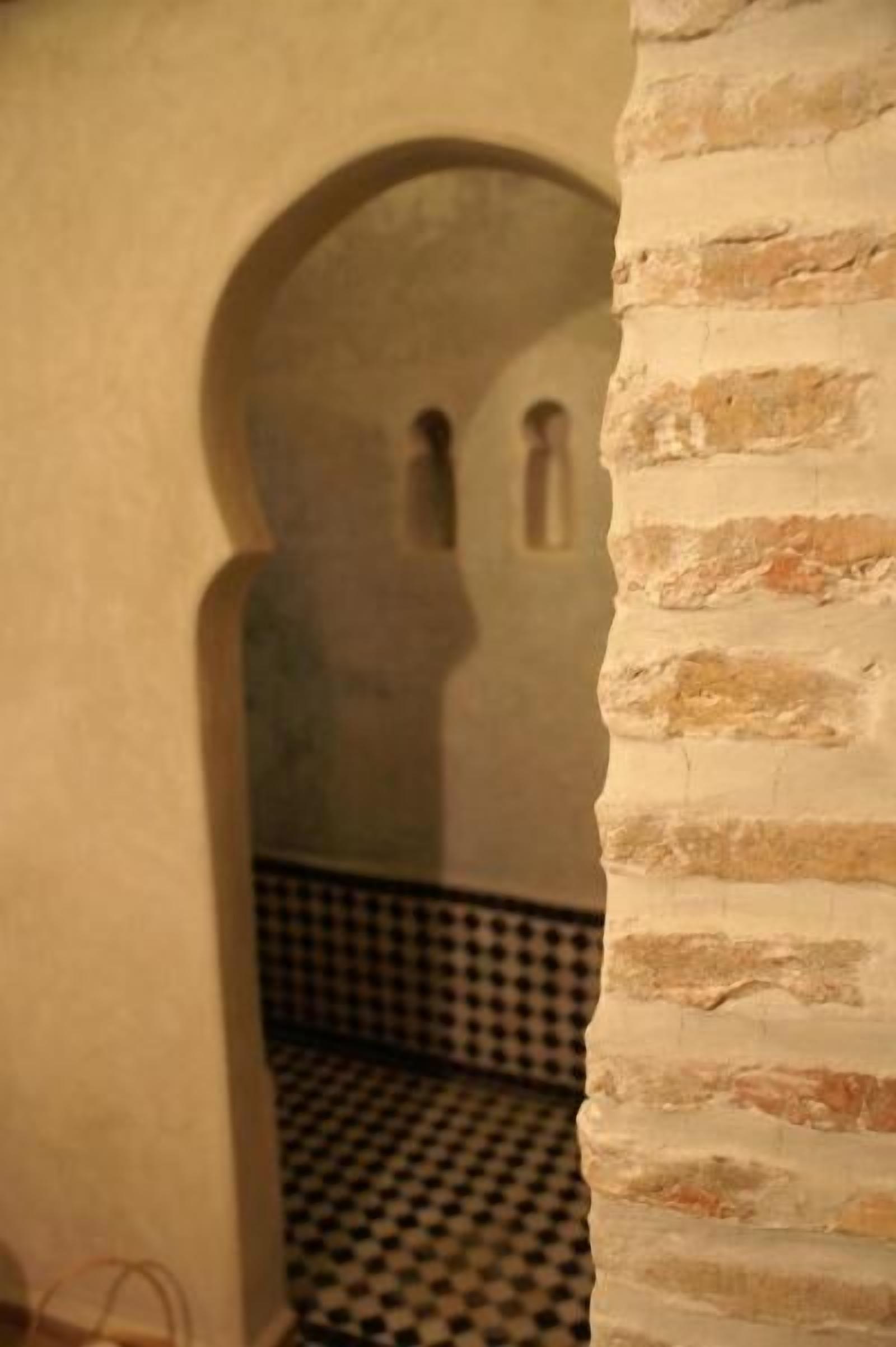 A room with a checkered floor, a brick wall, and a doorway leading to another room.