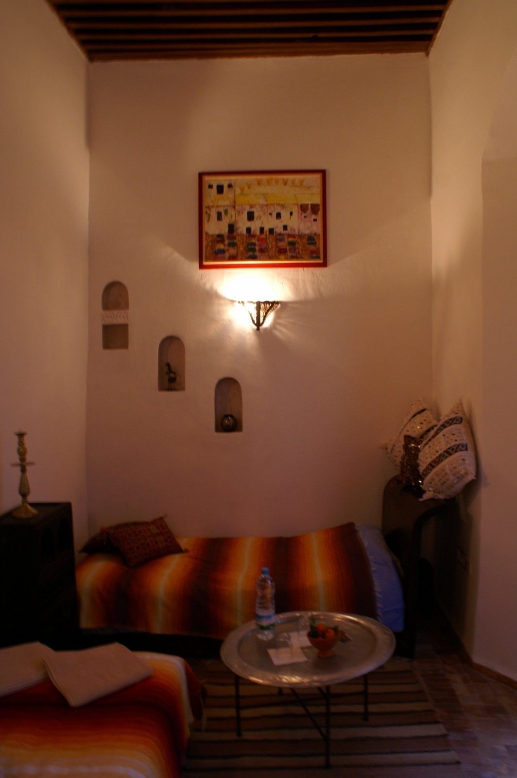 Ett mysigt rum med en soffa, ett litet bord med en vattenflaska, en lampa och en inramad tavla på väggen.