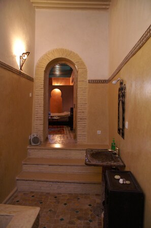 A narrow hallway with a tiled floor, a small sink, and a mirror on the wall.