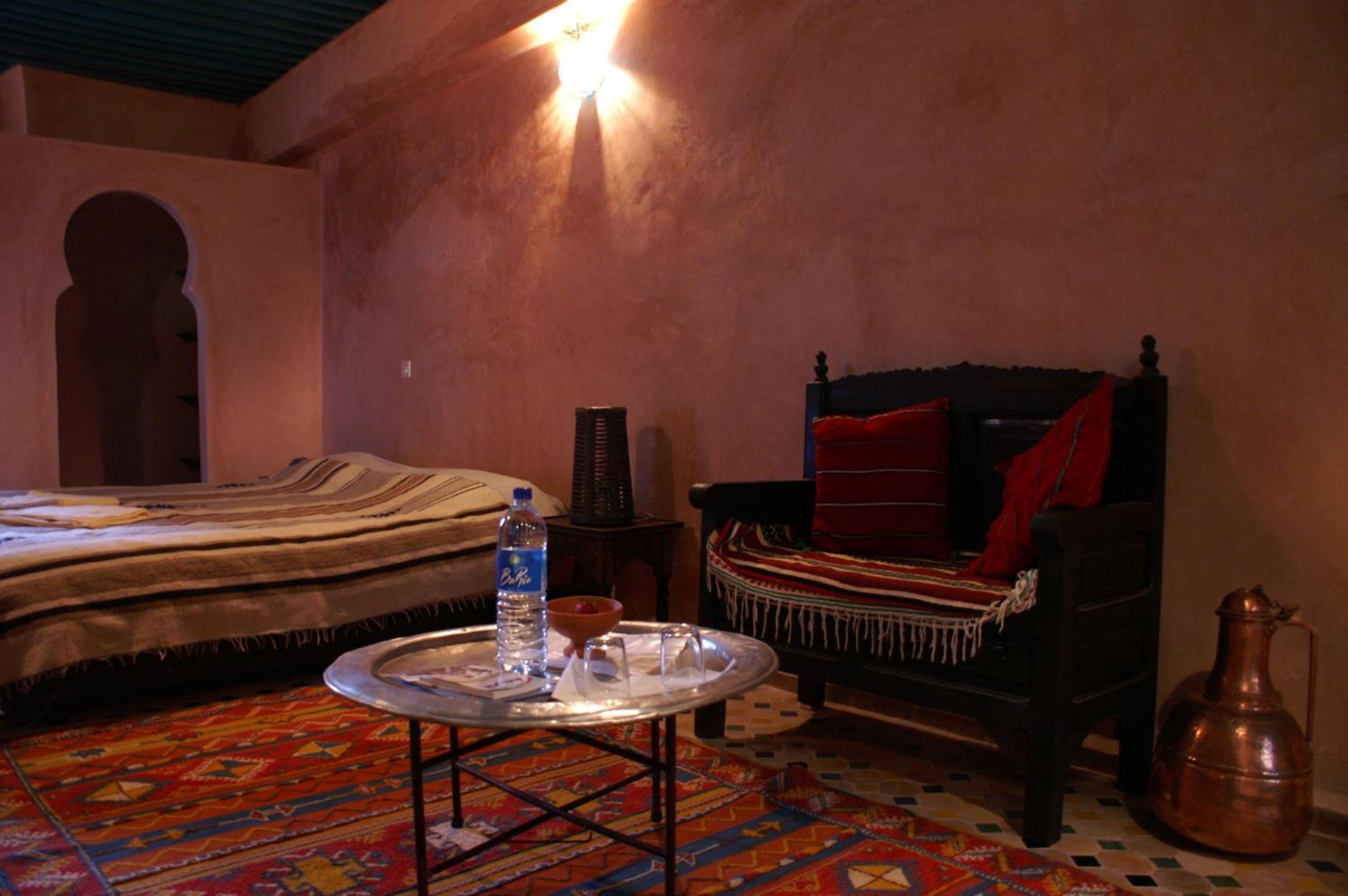 Een klassieke kamer met een bed, een fauteuil, een metalen dienblad met een waterfles en een koperen kan.