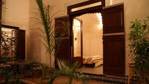 A traditional room with a bed, a sitting area with a table, and a large plant in the foreground. - Riad Felloussia (Meknes)