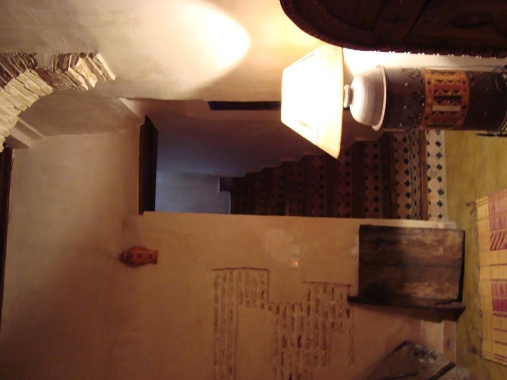 A narrow hallway with a lamp, a patterned wall, and a wooden door.
